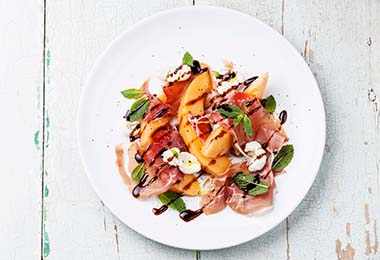 Una ensalada con una mezcla de sabores: vinagreta agria, frutas dulces, verduras amargas y jamón salado.