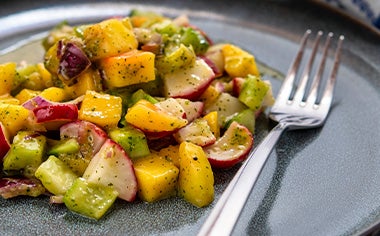 Una ensalada con mango y verduras, con su aderezo.