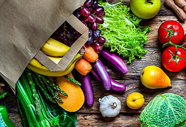 Una mesa con varias frutas y verduras. En el medio hay unas berenjenas alargadas.