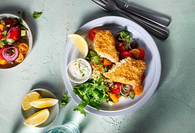 Ensalada mediterránea con pollo apanado, limón y salsa tártara en un plato blanco