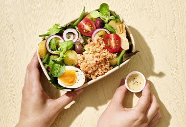 Ensalada Nicoise en una presentación portátil, con huevo duro, tomates, aceitunas y papas en un recipiente listo para llevar.