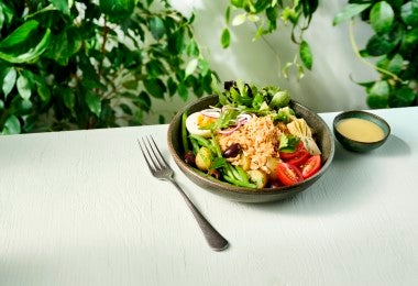 Ensalada Nicoise servida en un bowl oscuro, acompañada de un tenedor y vinagreta en un pequeño recipiente