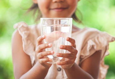 Niña sosteniendo un vaso de agua, un elemento vital para el buen descanso diario