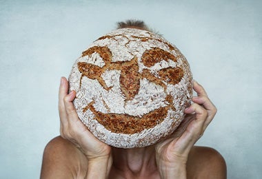 Cobertura de pan de masa madre con granos de centeno en unas manos.