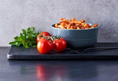 Pasta a la boloñesa junto a tres tomates maduros en un fondo grisáceo y negro