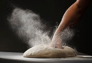 Una persona golpeando y amasando una masa de pizza con harina para celebrar su Día Mundial