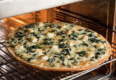 Pizza con queso, pollo y hojas verdes en un horno para celebrar su Día Mundial.