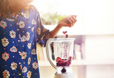 Mujer preparando acaí bowl añadiendo frutas en licuadora 