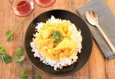 Ají de gallina servido sobre arroz blanco en un plato negro con hojas de cilantro fresco