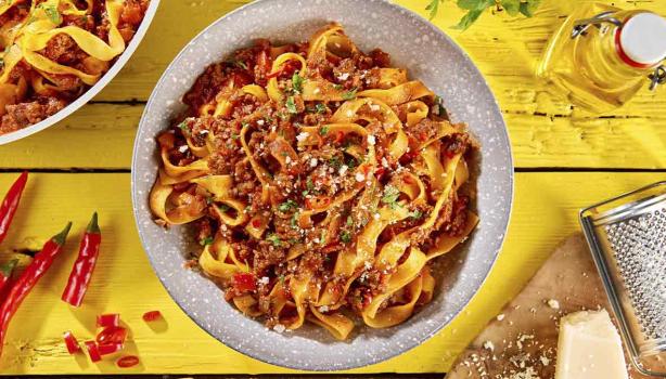 Pasta a la boloñesa con carne, queso parmesano y hierbas aromáticas sobre un fondo amarillo