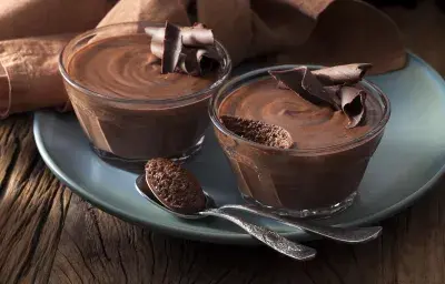 Foto de dos tazones pequeños con mousse de chocolate adentro encima de un plato azul Foto de dos tazones pequeños con mousse de chocolate adentro encima de un plato azul